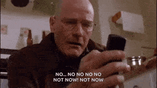 a man with glasses is holding a cell phone in his hand and saying `` no ... no no no not now ! not now ''