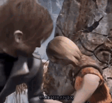 a man and woman are standing next to each other in front of a rock wall .