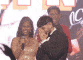 a man in a tuxedo is covering his face while a woman in a gold dress holds a microphone