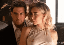 a man and a woman are standing next to each other and the woman is wearing a white dress and the man is wearing a suit