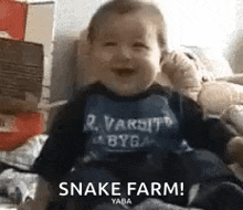 a baby is sitting on a bed wearing a bib that says `` snake farm ! ''