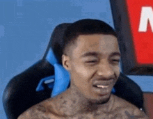 a man without a shirt is sitting in a gaming chair and smiling .