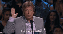 a man in a suit is talking into a microphone and says like a velociraptor