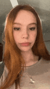 a young woman with red hair is wearing a necklace and a gray shirt .