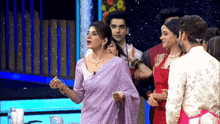 a group of people are standing on a stage and one of them is wearing a purple sari