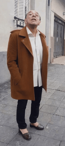 a man wearing a brown coat and black pants looks up
