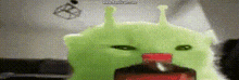 a green stuffed animal with a red nose is sitting next to a bottle .