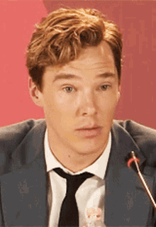 a man in a suit and tie is sitting at a microphone