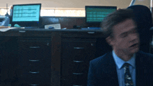 a man in a suit and tie sits in front of a computer monitor
