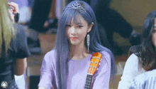 a girl with purple hair is holding a guitar and wearing a crown .