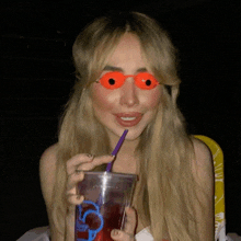 a woman wearing orange sunglasses is drinking from a cup