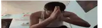 a man in a white tank top is covering his face with his hands .