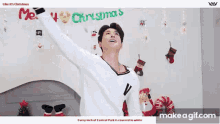 a man in a white sweater is standing in front of a sign that says merry christmas .