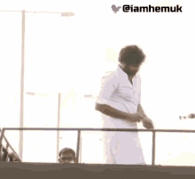 a man in a white shirt is standing on a railing with the hashtag @iamhemuk below him