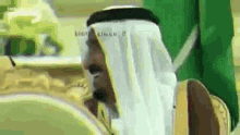 a man in a keffiyeh is sitting in front of a green flag and smiling .