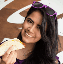 a woman wearing purple sunglasses holds a taco in her hand