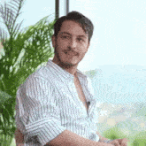 a man in a striped shirt is sitting in front of a palm tree .