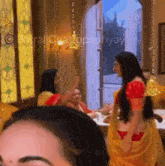 a group of women are standing in a room and one of them is wearing a yellow saree