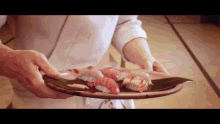 a person holding a plate of sushi on a table