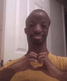 a man in a yellow shirt is smiling and making a heart with his hands .