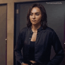 a woman in a black jacket is standing in front of a door with tamannah gifs written above her