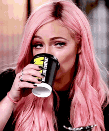 a woman with pink hair is drinking from a cup that says n on it