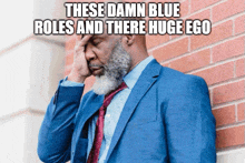 a man leaning against a brick wall with these damn blue roles and there huge ego above him