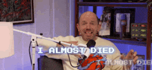 a bald man is sitting in front of a microphone with the words i almost died written on the screen behind him