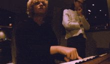 a woman playing a piano with a man behind her
