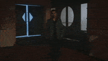 a man in a suit and black shirt is standing in a dark room .