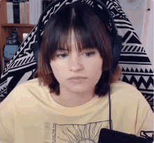 a young woman wearing headphones and a yellow t-shirt is sitting in front of a computer screen .