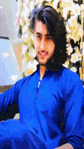 a man with long hair and a beard is wearing a blue shirt and smiling