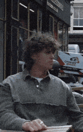 a young man sits at a table in front of a store that sells omega bikes
