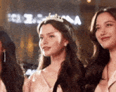 a woman with a tiara on her head stands next to two other women
