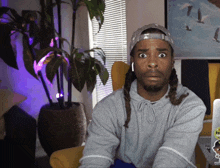 a man with dreadlocks wearing a hat and a grey hoodie