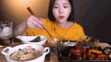 a woman in a yellow shirt is eating a variety of food with chopsticks