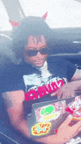 a man wearing devil horns is sitting in a car using a laptop .