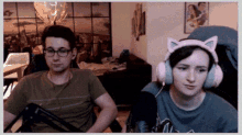 a man and a woman wearing cat ear headphones are sitting in front of a microphone