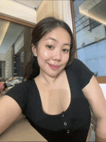 a woman in a black shirt is taking a selfie in front of a large window