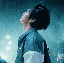 a man in a leather jacket stands in the rain looking up at the sky