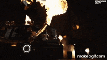 a man in a black leather jacket is standing in front of a fire .