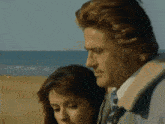 a man and a woman are standing on the beach looking at the ocean