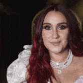 a woman with red hair is wearing a pearl necklace and a white top