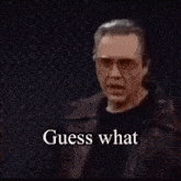 a man wearing glasses and a leather jacket is holding a gun and says and the only cure .