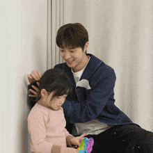 a man is brushing a little girl 's hair while holding a toy