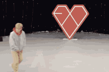 a person standing in front of a large red heart with the letter x on it