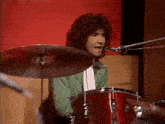 a man in a green shirt is playing drums in front of a red wall