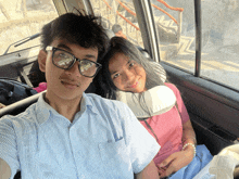 a boy and a girl are sitting in a car and the girl has a pillow on her neck