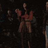 a woman in a pink pleated skirt stands in a crowd holding a red cup