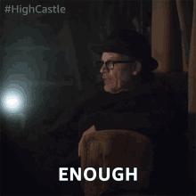 a man wearing a hat and glasses is sitting in a chair with the word enough below him